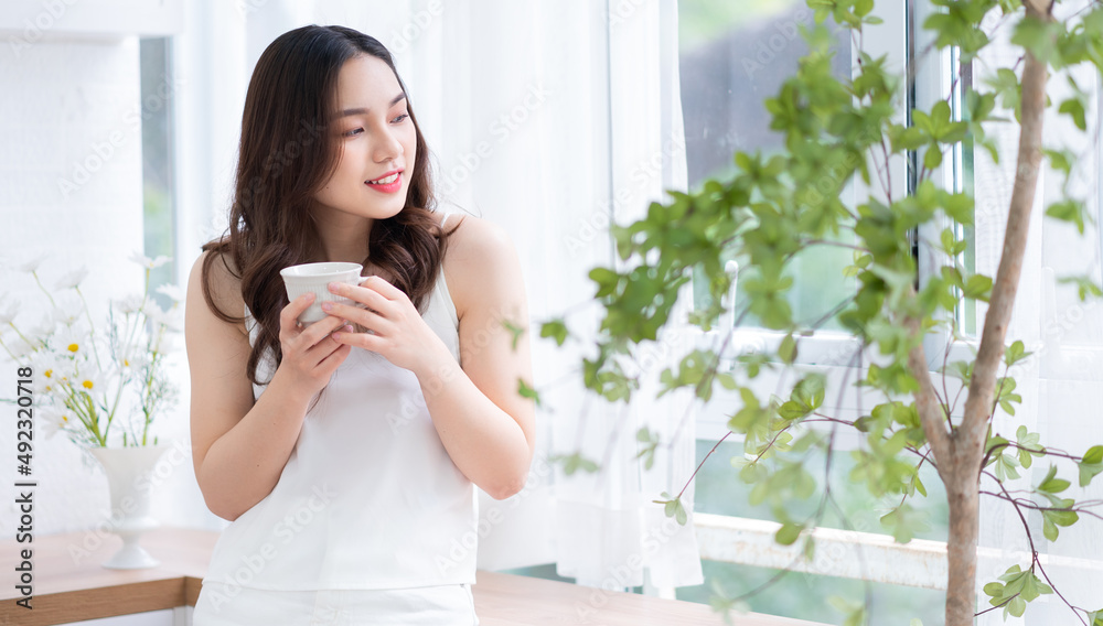 Image of beautiful young Asian woman drinking tea at home in the morning Image of beautiful young Asian woman drinking tea at home in the morning