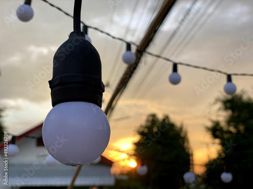 Vintage light bulb hang on cable. White and black bulb turn off under sunset sky.
