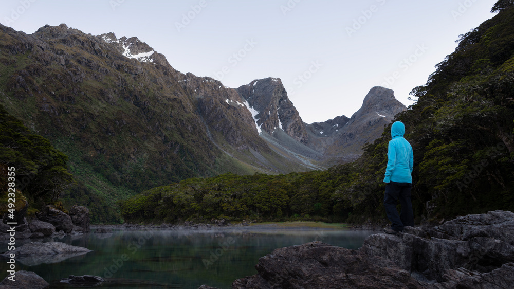 Naklejka premium A tramper standing on the rocks by the Lake Mackenzie at dawn, Routeburn Track, one of the great walks of New Zealand.