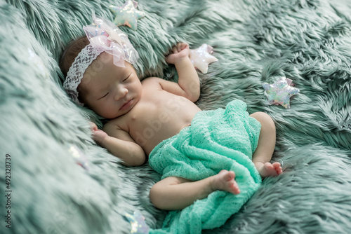 The newborn was wrapped in a green cloth with a headband and a bow was placed on a soft gray carpet. She is sleeping happily Soft focus