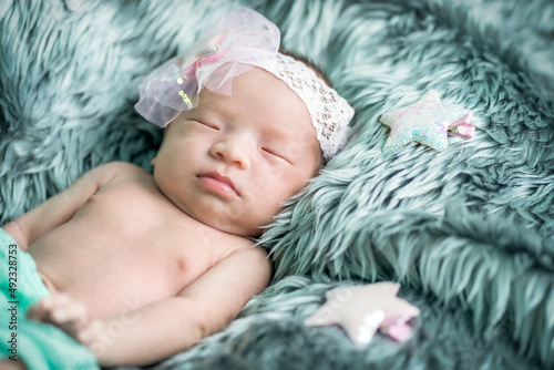 The newborn was wrapped in a green cloth with a headband and a bow was placed on a soft gray carpet. She is sleeping happily soft focus.