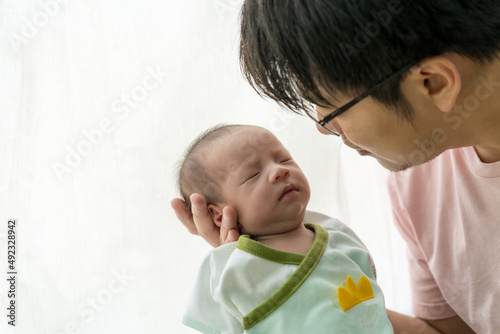 The father was nastily holding the newborn baby and sat beside a glass door with a curtain and white light. Give you a warm feeling