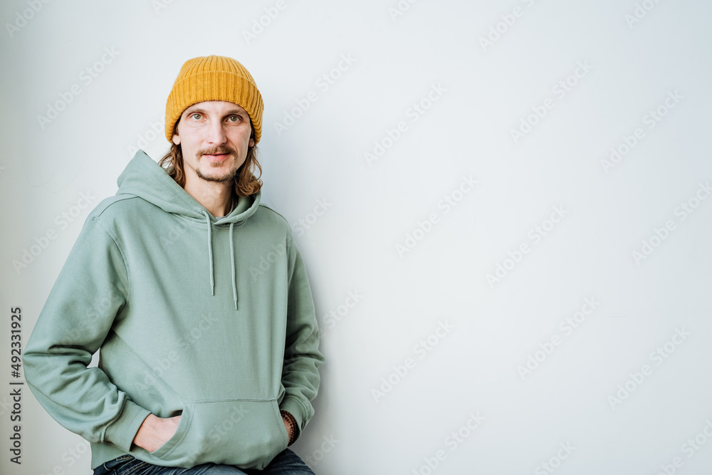 Portrait of a guy in a sweatshirt hands folded into a pocket on the head of a yellow hat, a man of European appearance hipster. Portrait of a guy in a sweatshirt hands folded into a pocket on the head of a yellow hat, a man of European appearance hipster.