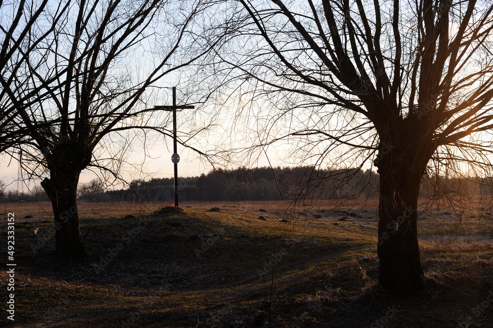 Rural landscape with willow trees and cross near a river in early spring during sunset in the evening before dusk near Chopin birth Place in Poland, Europe Rural landscape with willow trees and cross near a river in early spring during sunset in the evening before dusk near Chopin birth Place in Poland, Europe