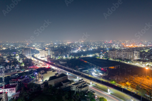 elevated metro track going across the screen over a lit road surrounded by buildings and metro train yard in distance with cityscape lights