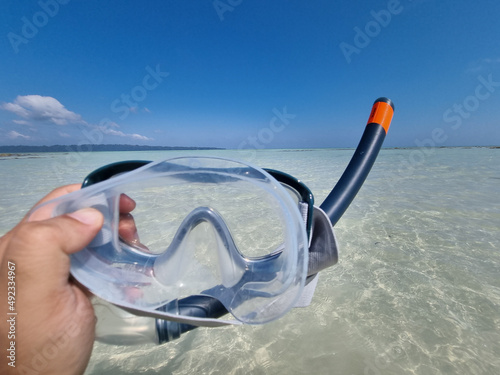 Panning shot holding out a snorkeling mask and breathing tube while going from the beach to the blue green waters at kala pathar beach andaman nicobar island India photo