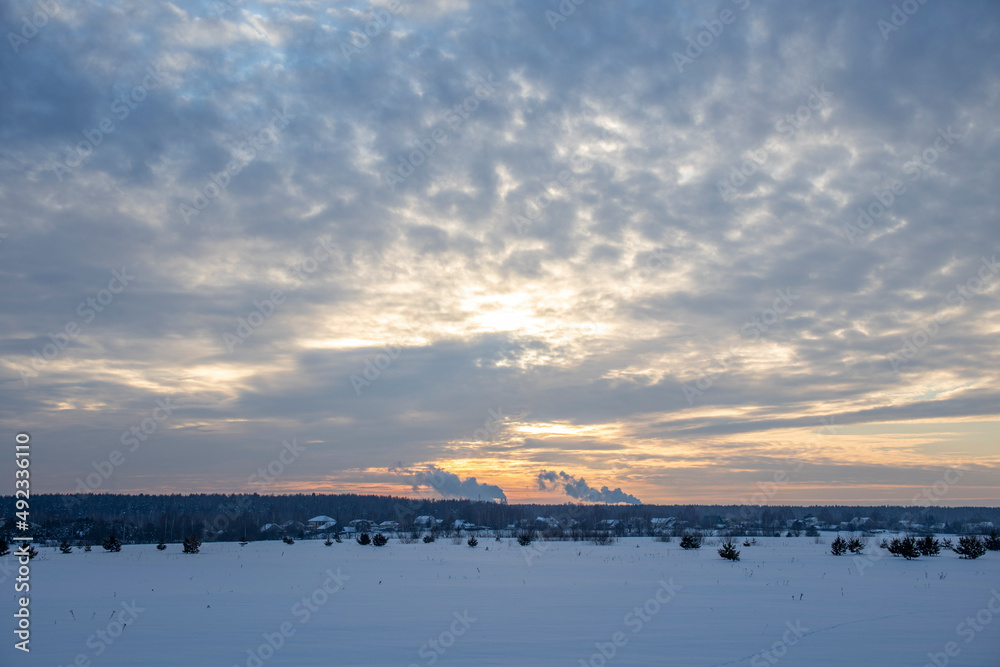 Obraz premium Winter minimalist landscape with colorful clouds in the sky and smoking chimneys on the horizon. winter tourism
