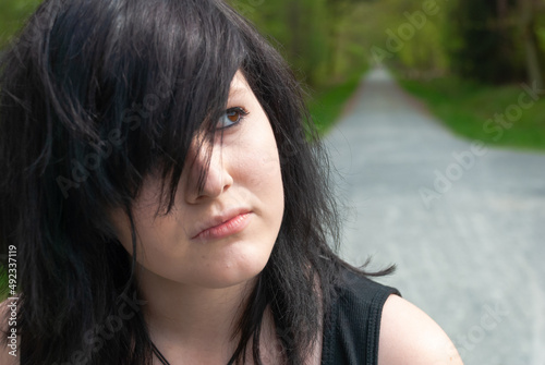 Punk emo girl  young adult with black hair and eyeliner  looking away  outdoors  close-up  horizontal