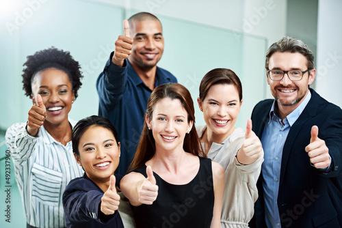 Stay positive, work hard and make it happen. High angle portrait of a group of businesspeople standing together and showing a thumbs up in the office.