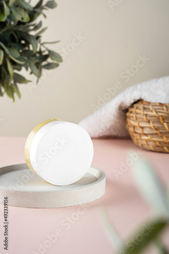 An open jar with Lanolin, a grease from sheep wool. Acts as a skin ointment, water-proofing wax, and for washing laundry. pink background, soft towel and green plant on the bathroom background photo