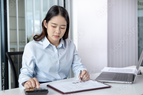 Businesswoman presses a calculator to calculate earnings and analyze company earnings in his private office, Information in finance and accounting, Company performance and revenue. © Puwasit Inyavileart