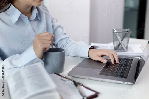 Businesswoman working on laptop and sipping coffee comfortably  Sitting in a private office  Using computers to conduct financial transactions  World of technology and internet  Work lifestyle.