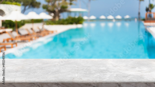 Fotografia Empty white marble stone table top and blurred swimming pool in tropical resort in summer banner background - can used for display or montage your products