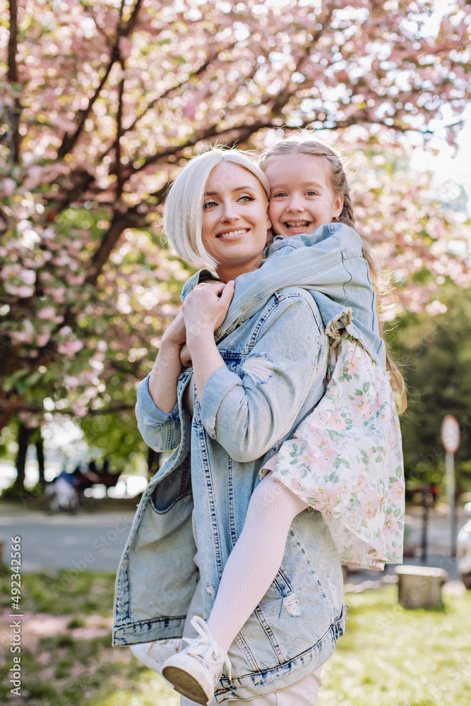 Little girl hugged her mother on a background of sakura in the garden.