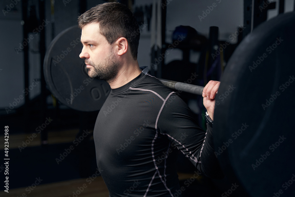 Athletic man doing exercise with barbell in gym