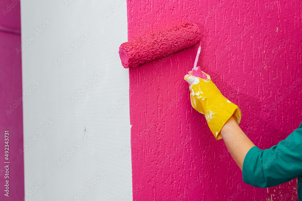 A girl paints a wall close-up with a roller in pink in her new apartment. Renovation of the interior and a new apartment. Housewarming and a desirable mortgage.