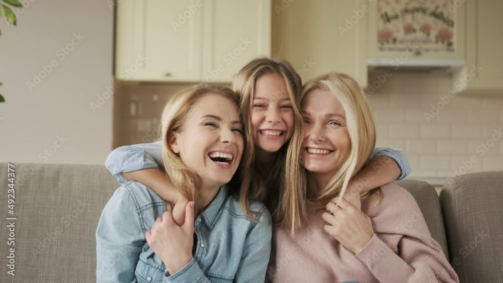 three generations of women look at camera, cute little girl hug mom and granny enjoy time at home, smiling mother, daughter and grandmother