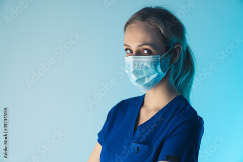Serious health care female worker looking at camera, wearing surgical mask to prevent bacteria and viruses from spreading. High quality photo