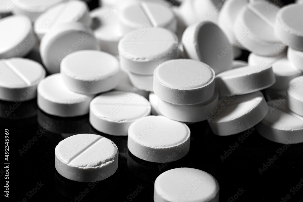 Close up of white painkiller tablet on a reflective black background Close up of white painkiller tablet on a reflective black background
