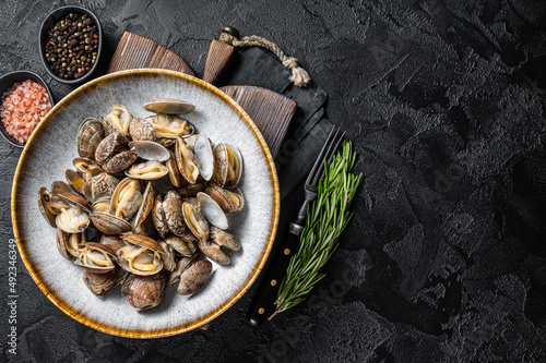 Steamed cooked shells Clams vongole in a plate with herbs. Black background. Top view. Copy space photo