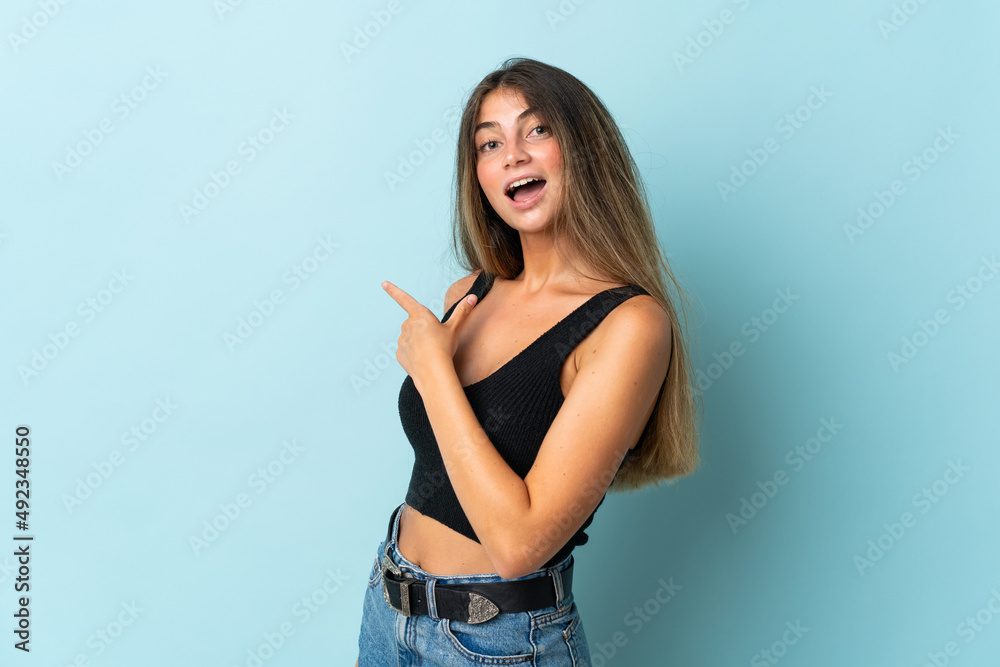 Young caucasian woman isolated on blue background surprised and pointing side Young caucasian woman isolated on blue background surprised and pointing side