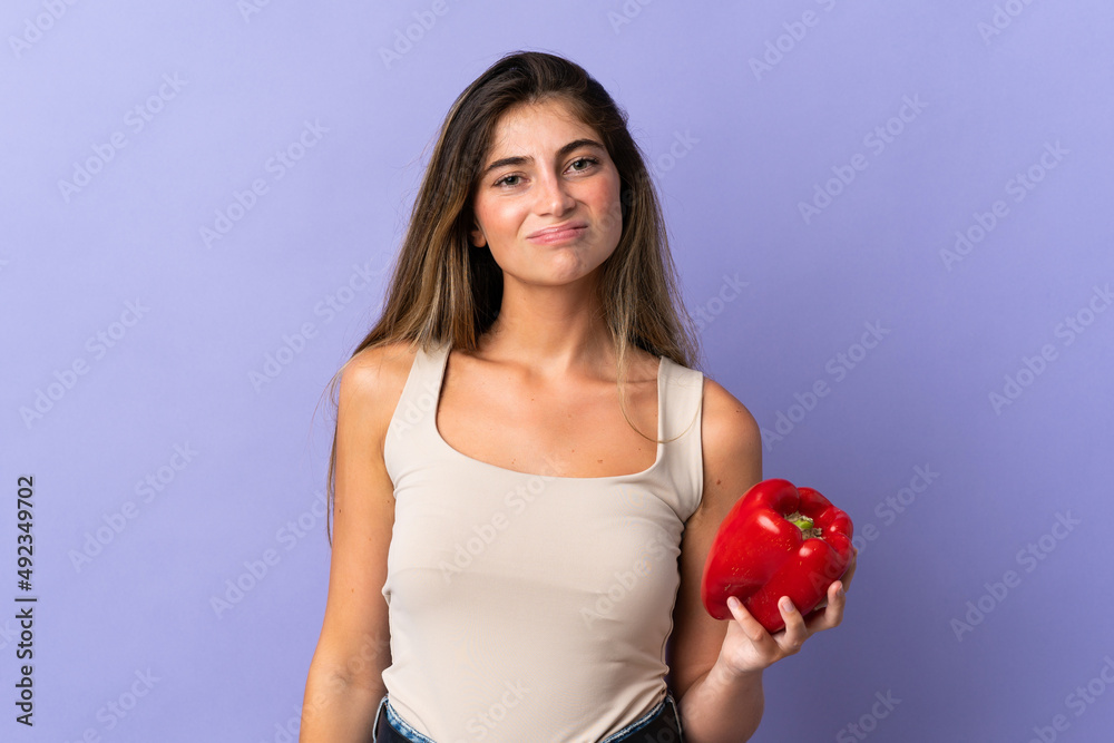 Young woman holding a pepper isolated on purple background with sad expression Young woman holding a pepper isolated on purple background with sad expression