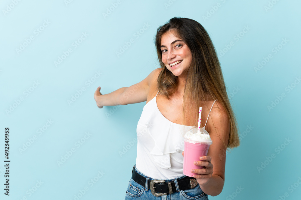 Young woman with strawberry milkshake isolated on blue background extending hands to the side for inviting to come