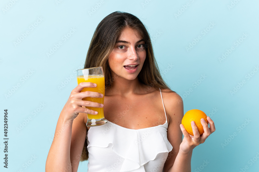 Young caucasian woman isolated on blue background holding an orange and an orange juice Young caucasian woman isolated on blue background holding an orange and an orange juice