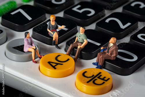 Miniature 4 people sitting on a white calculator. meeting or discussion using as business concept. Macro