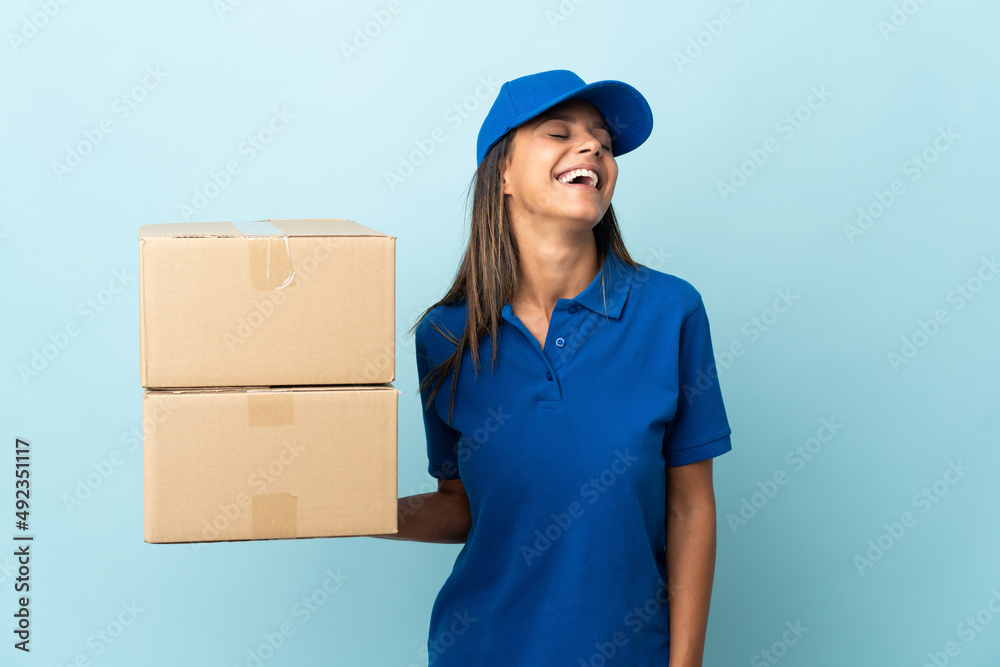 Young delivery woman isolated on blue background laughing Young delivery woman isolated on blue background laughing