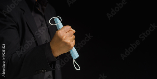 Businessman holding a medical mask in his fist while standing over a black background