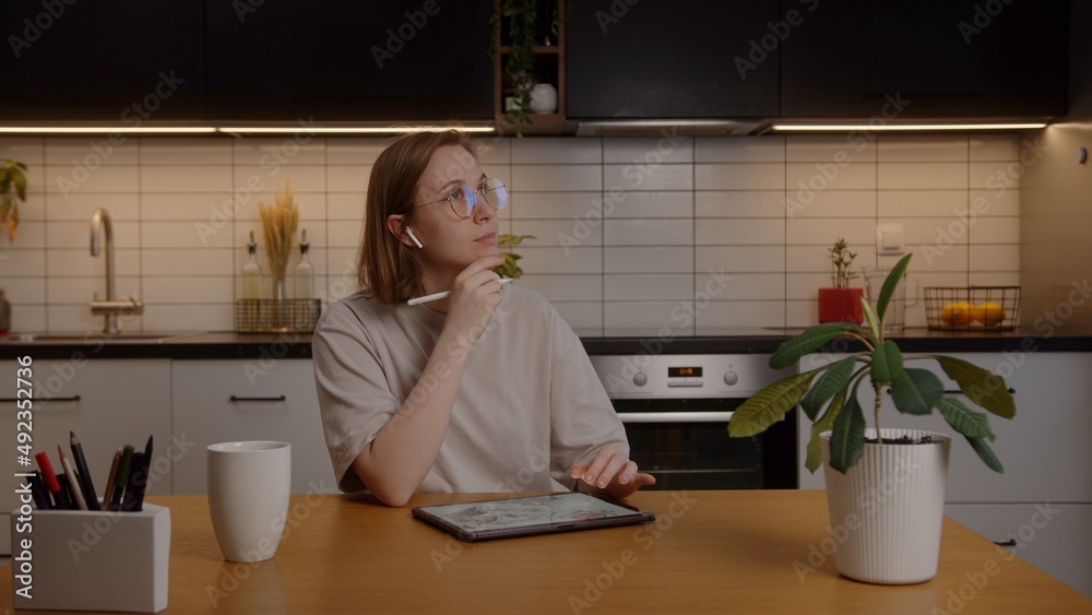 Thoughtful creative european girl designer working at home in the kitchen using a tablet