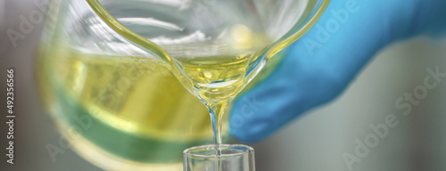 Scientist hand wearing glove pouring petroleum yellow lubricating oil high viscosity into test tube in the laboratory. Automotive and industrial oil technology concept