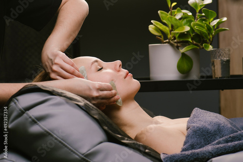 Gua sha. Side view of a woman receiving facial massage in a beauty salon