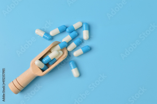 Wooden scoop and pill capsules isolated on a blue background. Copy space for the text.