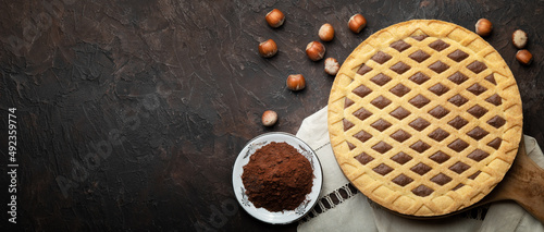 Tart with hazelnuts and cocoa powder on wooden cutting board. Top view on brown plaster background, space for text, flat lay. photo