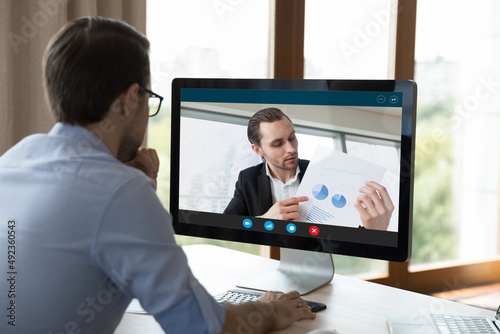 Photography Focused millennial businessman ceo executive sit at workplace before pc screen talk to colleague discuss marketing report with subordinate analyze sales results by video call