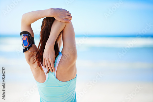 Preparing for a run. Rearview shot of a young woman stretching before a work out on the beach.