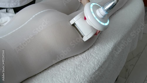 LPG massage in a beauty salon. A beautiful client in a special white suit receiving an anti-cellulite massage in a beauty salon. A doctor manipulating a hardware cosmetology device. Body care