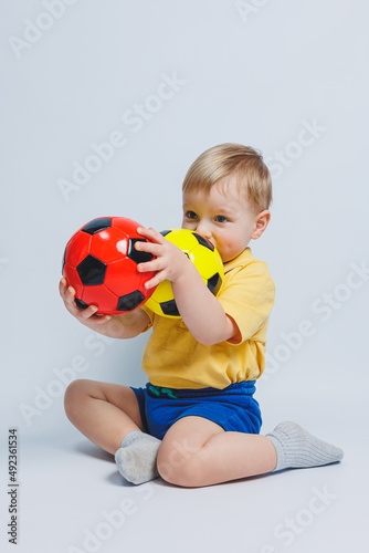 Boy fan holding a soccer ball in his hands, isolated on a white background. newbie child in football, sport for kids. Little athlete. Yellow and blue football kit for kids