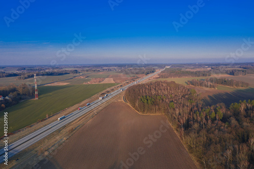 Droga na równinie pokrytej łąkami i polami uprawnymi. Jest słoneczny dzień. Widok z dużej wysokości, zdjęcie wykonano z użyciem drona.
