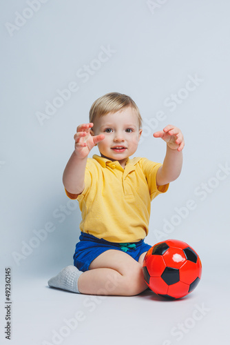 Boy fan holding a soccer ball in his hands, isolated on a white background. newbie child in football, sport for kids. Little athlete. Yellow and blue football kit for kids