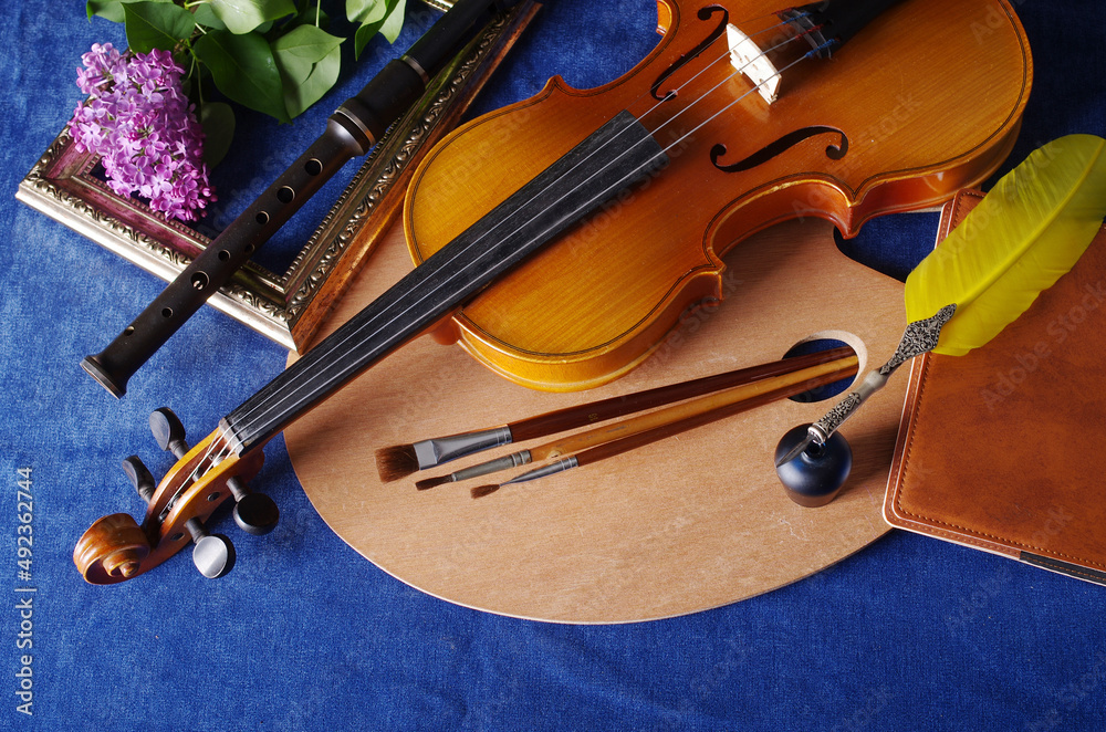 Fototapeta premium Flowers in vases, violin, art palette and brushes on a table with a blue tablecloth.