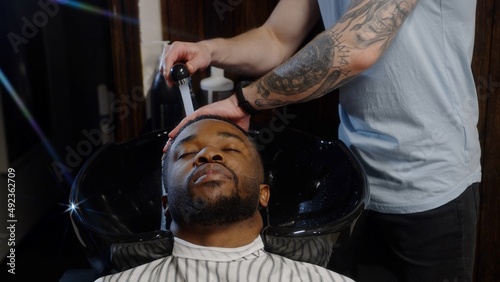 Barber washes shampoo off the head of an African American in a special sink