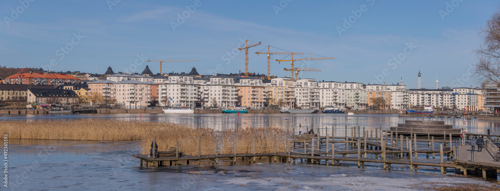 Panorama view at the icy bay Hammarby sjö with floes, apartment building and recreation area with commuting ferries a sunny winter day in Stockholm