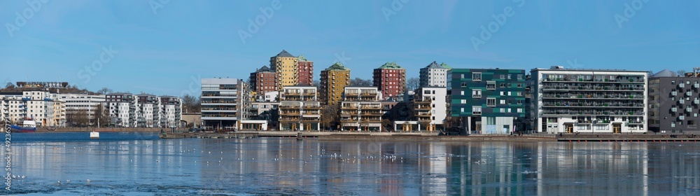 Panorama view at the icy bay Hammarby sjö with floes, apartment building and recreation area with commuting ferries a sunny winter day in Stockholm Panorama view at the icy bay Hammarby sjö with floes, apartment building and recreation area with commuting ferries a sunny winter day in Stockholm
