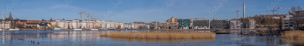 Panorama view at the icy bay Hammarby sjö with floes, apartment building and recreation area with commuting ferries a sunny winter day in Stockholm