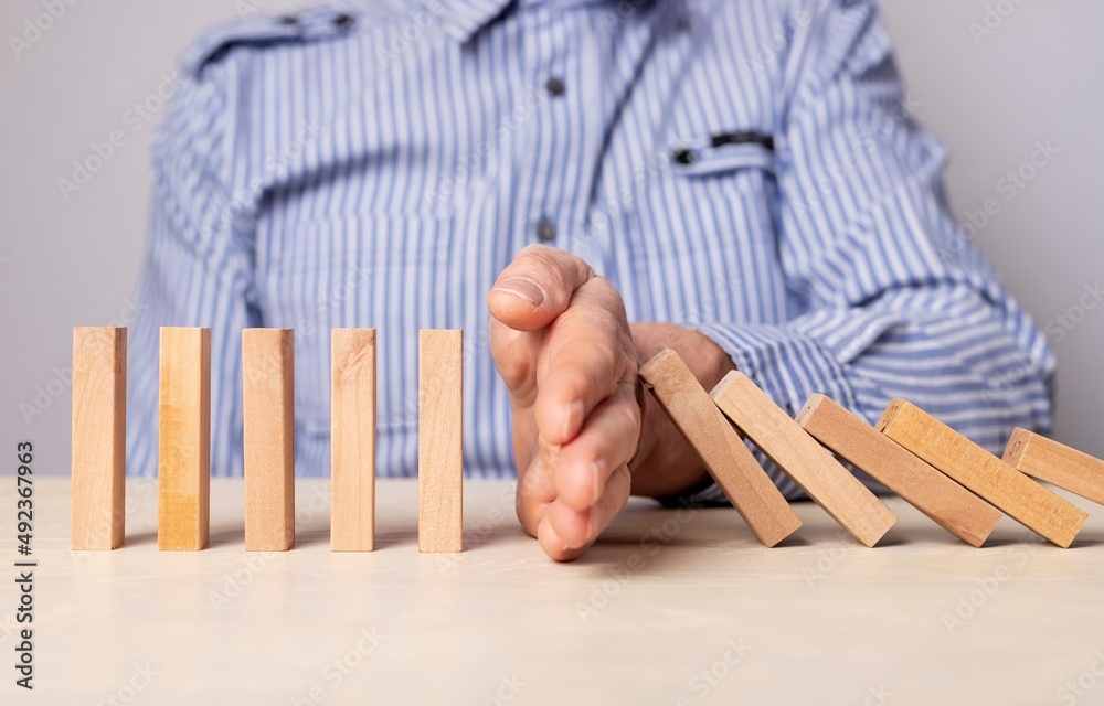 Insurance and business risk management concept. Businessman hand closeup protecting wood blocks from falling. Domino effect stopping. High quality photo Insurance and business risk management concept. Businessman hand closeup protecting wood blocks from falling. Domino effect stopping. High quality photo