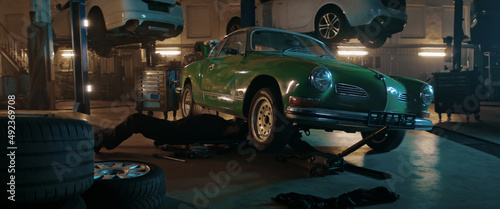 50s Adult Caucasian male mechanic repairing a vintage old car in a workshop, working under car bottom