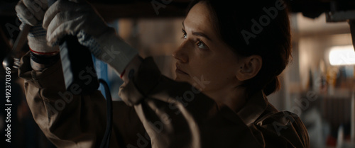 CU portrait of Caucasian female mechanic repairing a car in a workshop, working under car bottom. Shot with 2x anamorphic lens © supamotion